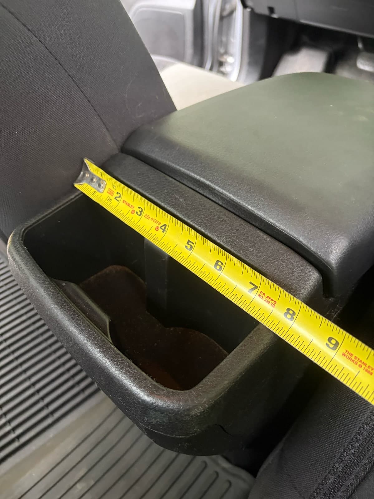 A tape measure crosses the long span of the Tacoma rear cup-holder opening.