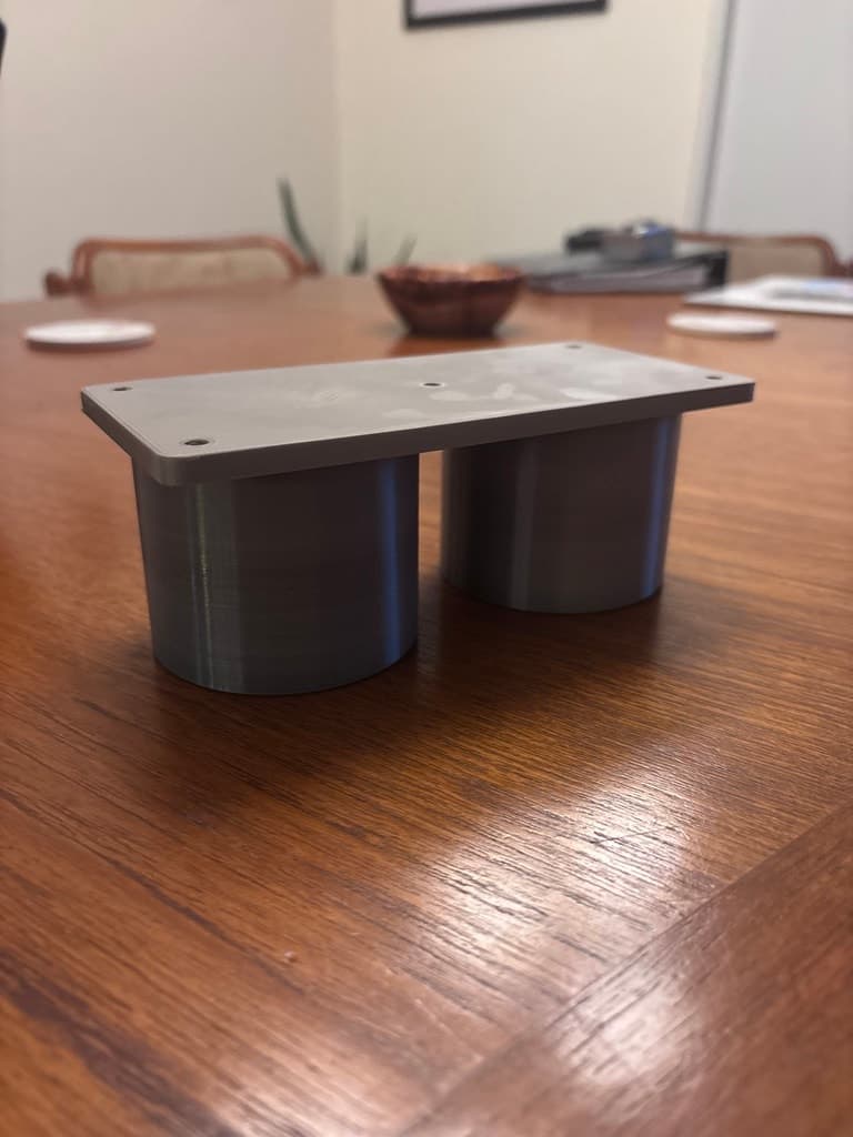 The finished gray cup-holder mount on a wooden table, with a five-hole rectangular platform above two cylindrical inserts.