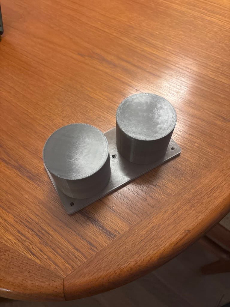 The printed mount turned upside down, showing two flat-ended cylindrical inserts beneath the plate.
