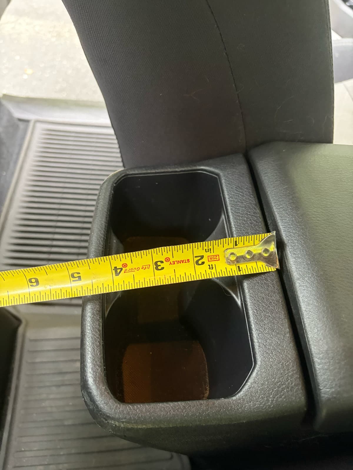 A tape measure crosses the short span of the Tacoma rear cup-holder opening.