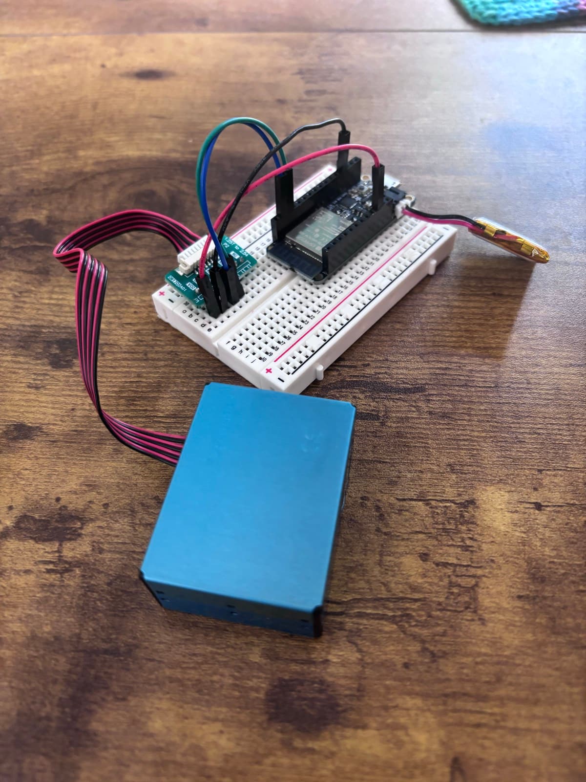 Close-up of four jumper wires running from the Plantower sensor's breakout board, across the breadboard, into the Feather's pins.