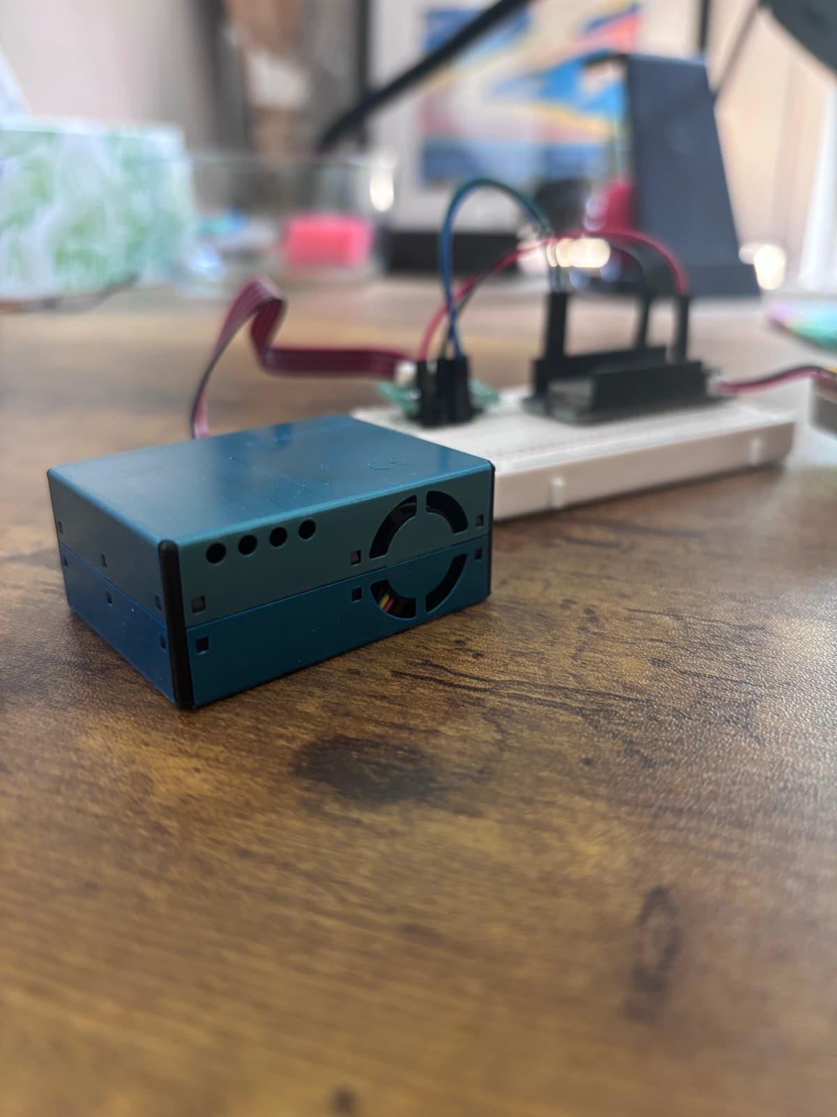The Plantower sensor's blue metal enclosure with its intake fan visible, sitting in front of the breadboard and Feather.